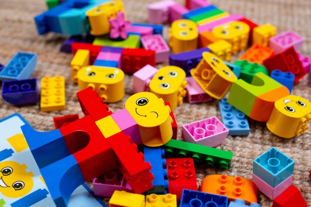 LEGO bricks lie scattered on a rattan rug alongside the shape of a person made from LEGO with a winky face.