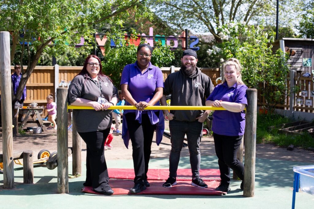 Members of staff at Storkway Nursery stand together in the playground and smile at the camera.